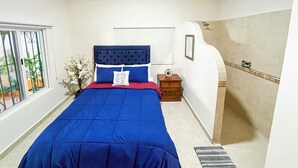 A bedroom with a large bed, a nightstand, a window with a view, and a bathroom with a shower.