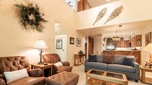 A living room with a brown leather sofa, a matching ottoman, a glass coffee table, and a grey sofa with blue cushions. - Snowbound at Snow Flower — 2 Bedrooms + Loft, Heated Pool, Hot Tub & Fitness! (Park City)