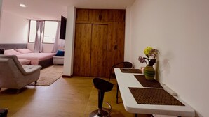 A modern living room with a sofa, a dining table with chairs, a wooden wardrobe, and a vase with flowers on the wall.