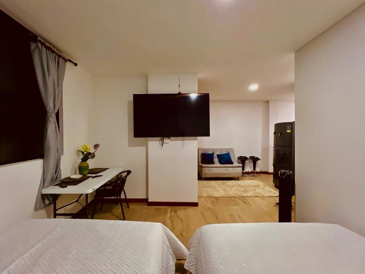 Et hotelværelse med to senge, et fjernsyn, et skrivebord med stol, en sofa og et lille bord med en vase.