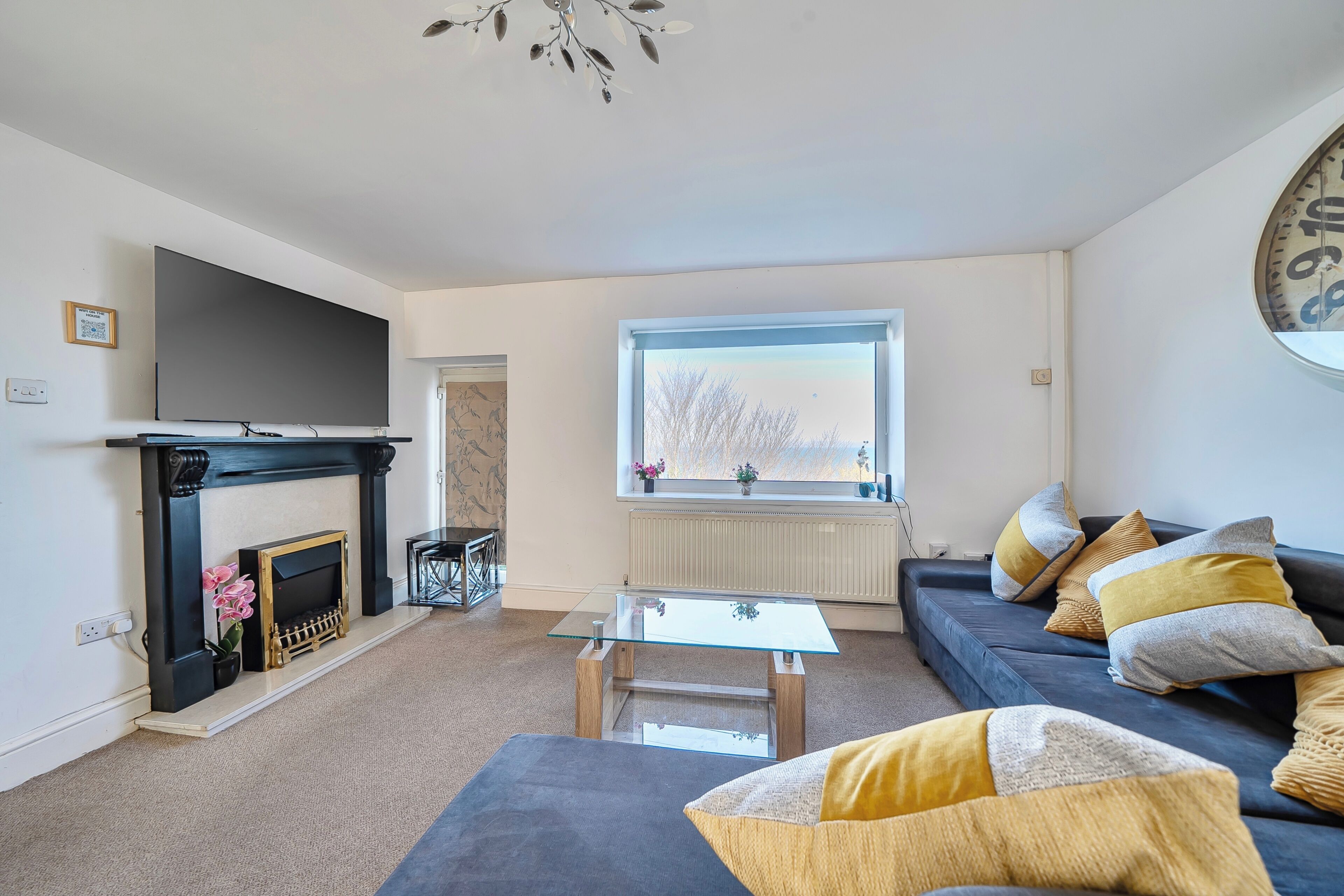 A living room with a fireplace, a sofa, a glass coffee table, and a large window.
