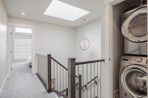 A laundry room with a washing machine and dryer, a skylight, and a staircase with a railing.