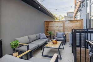 An outdoor seating area with a grey sofa, a wooden table, and a potted plant.