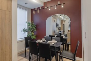 A dining area with a table set for four, a potted plant, and a view into a kitchen through an archway.