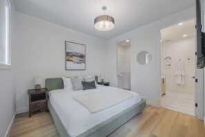 A bedroom with a bed, bedside tables, a wall-mounted mirror, and a door leading to a bathroom.