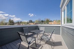 A rooftop patio with a table and chairs, a view of buildings in the distance, and a clear sky.