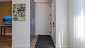Un pasillo con piso de madera, un recibidor con alfombra oscura, un cuadro en la pared y un televisor sobre un mueble.