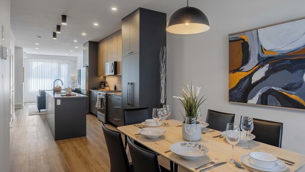 Un comedor moderno con una isla central, sillas negras y un cuadro abstracto grande en la pared.