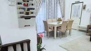 Een woonkamer met een eettafel, stoelen, een bank, een airconditioner, een wandheater, een boekenplank en een potplant.