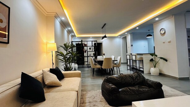 A modern living room with a sofa, a black leather couch, and a dining area with chairs and a table. - Addis Home & Comfort - Sarbet - Addis Ababa (Addis Ababa)
