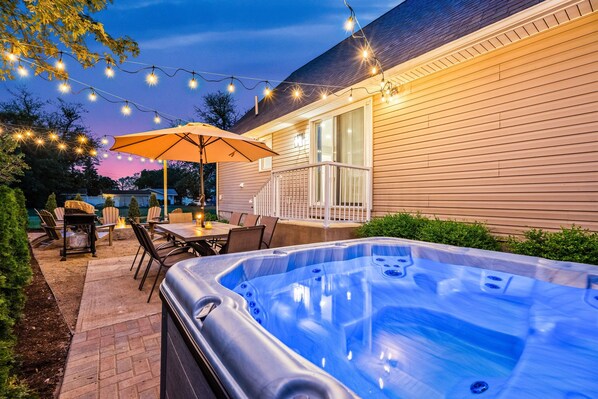 Eine Terrasse im Freien mit Whirlpool, Lichterkette und Gartenmöbeln.