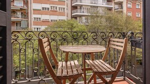 Un balcón con dos sillas de madera y una mesa, rodeado por una barandilla de hierro forjado.