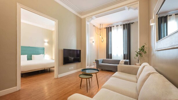 Una sala de estar con sofá, televisión, una mesita y una cama con cabecera color turquesa.