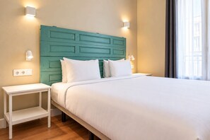 A hotel room with a bed, bedside tables, and wall-mounted lighting.