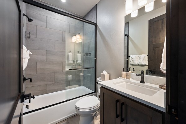 A modern bathroom with a glass-enclosed shower, a white toilet, and a vanity with a mirror.