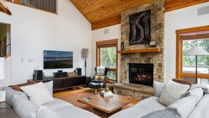 A modern living room with a stone fireplace, a large window, and a cozy seating area. - Silver Lining Chateau 374 I Amazing Views I Private Hot Tub I Bunk Room I Discounted Attractions (Tabernash)
