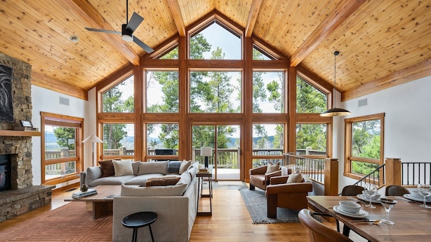 A spacious living room with a large fireplace, wooden ceiling, and large windows offering a view of trees. - Silver Lining Chateau 374 I Amazing Views I Private Hot Tub I Bunk Room I Discounted Attractions (Tabernash)