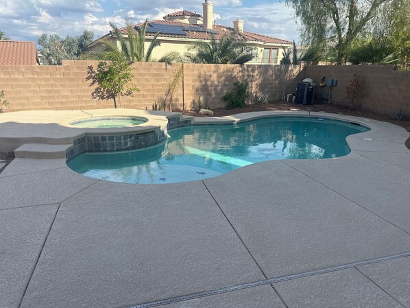 Une piscine avec un jacuzzi, entourée d’un mur de briques et de palmiers.