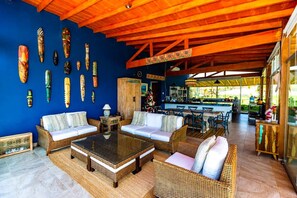 A spacious living area with wicker furniture, a wooden ceiling, and a bar area visible in the background.
