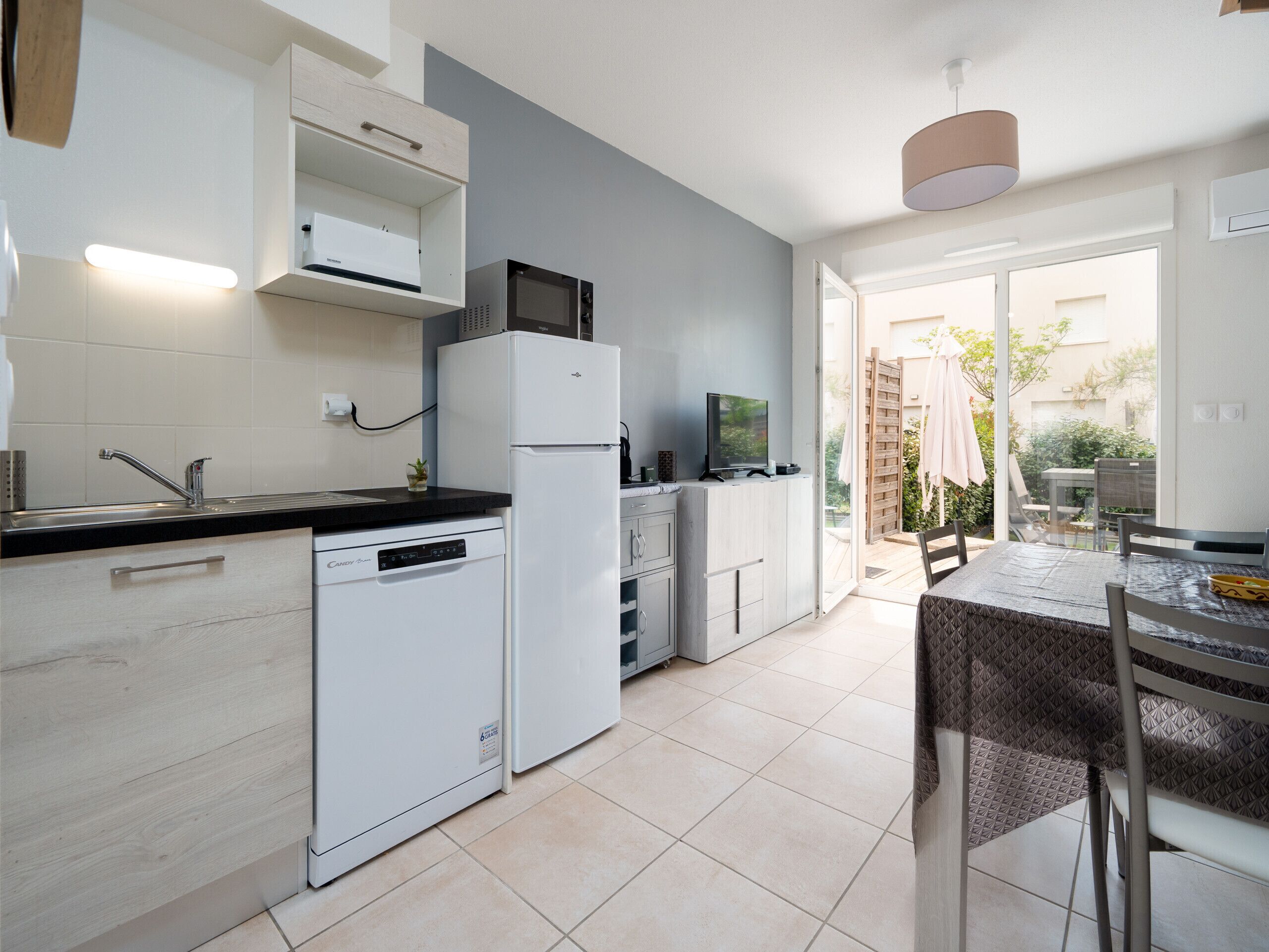 A modern kitchen with white cabinetry, a built-in dishwasher, and a dining area with a table and chairs.