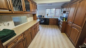 Une cuisine avec des meubles en bois, un four à micro-ondes, un lave-vaisselle et une fenêtre avec des stores.