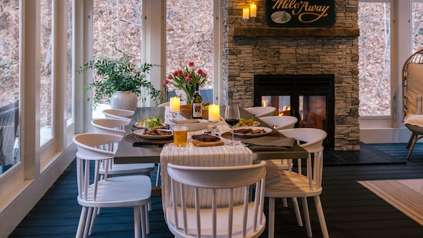 A dining area with a stone fireplace, white chairs, and a table set for four.