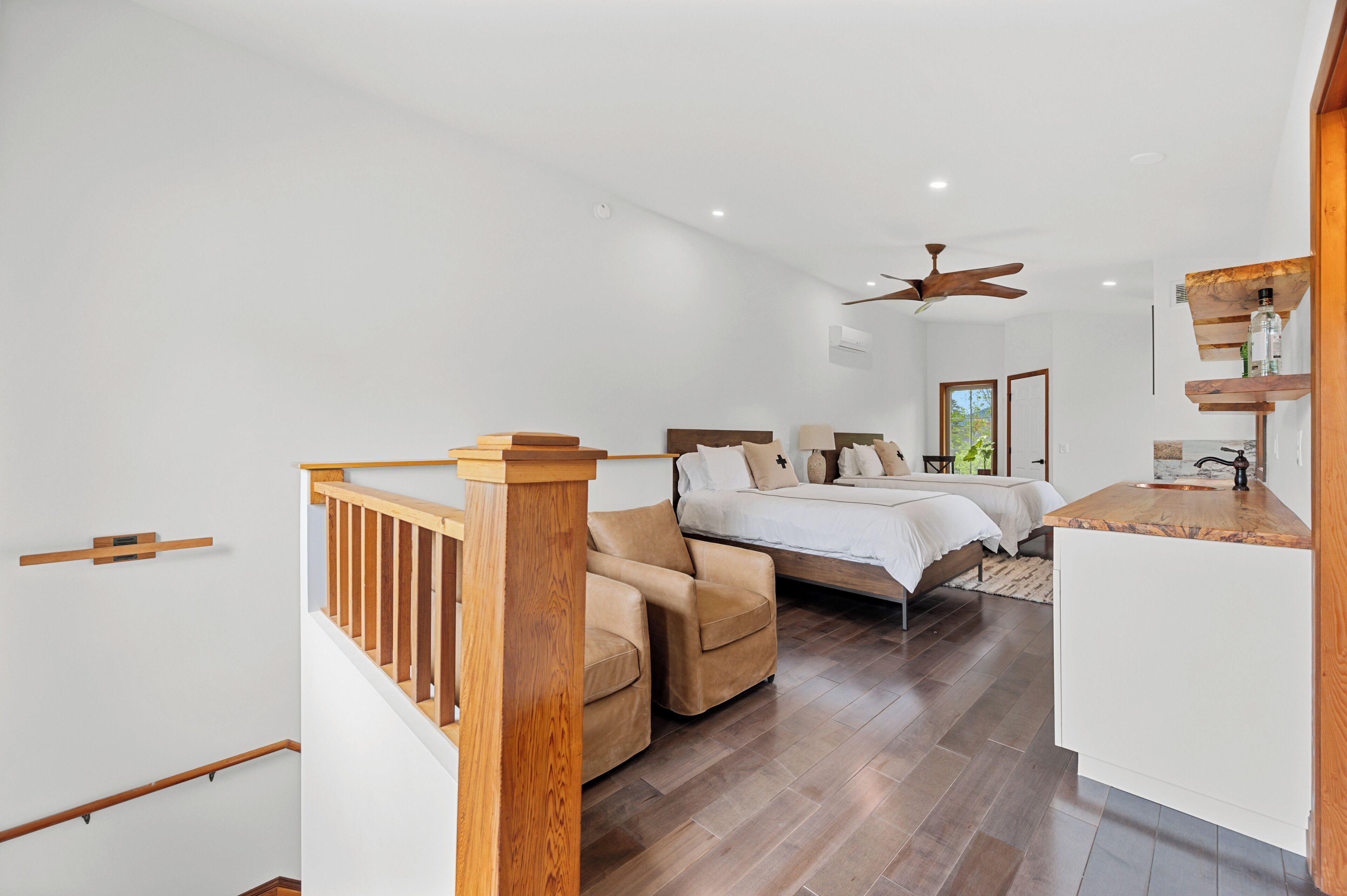 Une chambre avec un lit, une chaise, un escalier en bois et un petit coin cuisine.