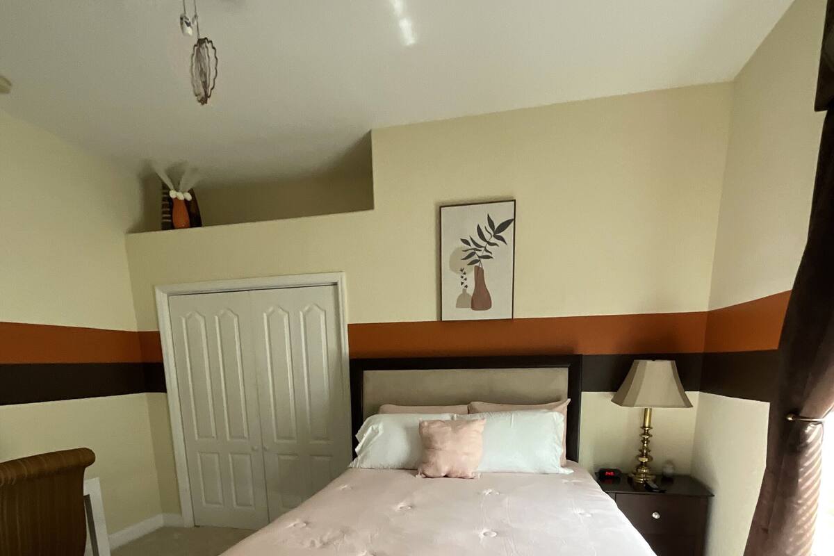 A bedroom with a bed, a bedside table, a lamp, a door, and a ceiling fan.