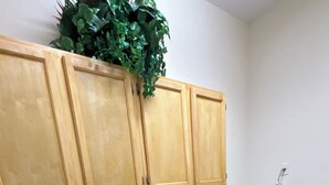 A laundry room with two washing machines, wooden cabinets above, and a sign on the floor. - Quiet Lakeview Home (Wesley Chapel)