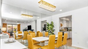 A modern dining area with a white table and yellow chairs, a chandelier, and a view of the kitchen and living area.