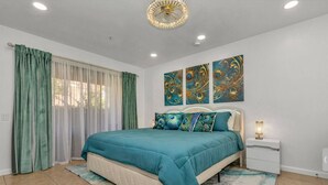 A bedroom with a bed, curtains, a nightstand, and wall art.