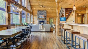 A spacious kitchen with a stone fireplace, wooden beams, and large windows. - Hot Tub Soaks, Scenic Vistas, Starlit S'mores, Game Nights & Outdoor Fun - Little Creek Cabin (Blue Ridge)