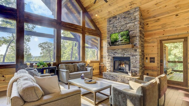 A cozy living room with a stone fireplace, large windows, and comfortable seating. - Hot Tub Soaks, Scenic Vistas, Starlit S'mores, Game Nights & Outdoor Fun - Little Creek Cabin (Blue Ridge)