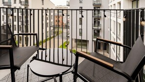 Un balcón con dos sillas y una mesita, con vista a un patio y edificios al fondo.