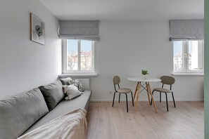 A modern living room with a grey sofa, two chairs, a small table, and a window with a view of buildings.