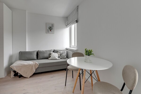 A modern living room with a grey sofa, a round white table, and a window with a view.
