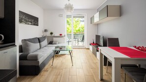 A modern living room with a sofa, a glass coffee table, a dining table with a red runner, and a kitchen area with a refrigerator and cabinets. - Włochy Popularna Charming Studio (Warszawa)