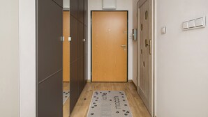 A narrow hallway with a wooden door at the end, a mat with text, and a wall-mounted light fixture. - Włochy Popularna Charming Studio (Warszawa)