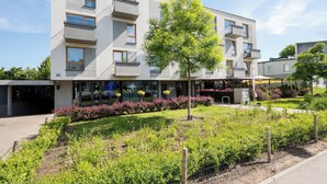 A modern multi-story building with balconies, a landscaped garden, and a café at the ground level. - Włochy Popularna Charming Studio (Warszawa)