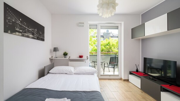 A modern bedroom with a bed, a TV, and a balcony with a view of greenery. - Włochy Popularna Charming Studio (Warszawa)