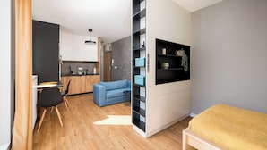 Een modern appartement met een keuken, een zithoek met een bank, een eethoek met een tafel en stoelen, en een bed met een gele deken.