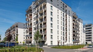 Een meerlaags woongebouw met balkons, een hekpoort en een parkeerplaats.