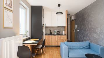 Un espacio habitable compacto con kitchenette, comedor y zona de estar con sofá y mesa de centro.