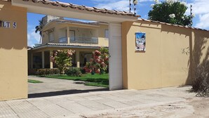 L’entrée d’une auberge de jeunesse, avec un chemin dallé, un balcon et un jardin agrémenté de fleurs roses.