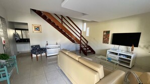 Un salon moderne avec un canapé beige, une table basse en verre, un téléviseur et un escalier.