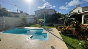 Une piscine dotée d’une terrasse carrelée, entourée d’une pelouse bien entretenue et de diverses plantes.