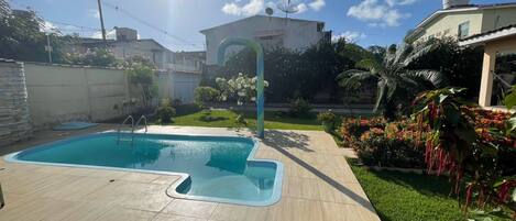 A swimming pool with a tiled deck, surrounded by a well-maintained lawn and various plants.