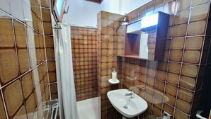 Ein Badezimmer mit braunen Fliesenwänden, einem weißen Waschbecken und einer Duschkabine.