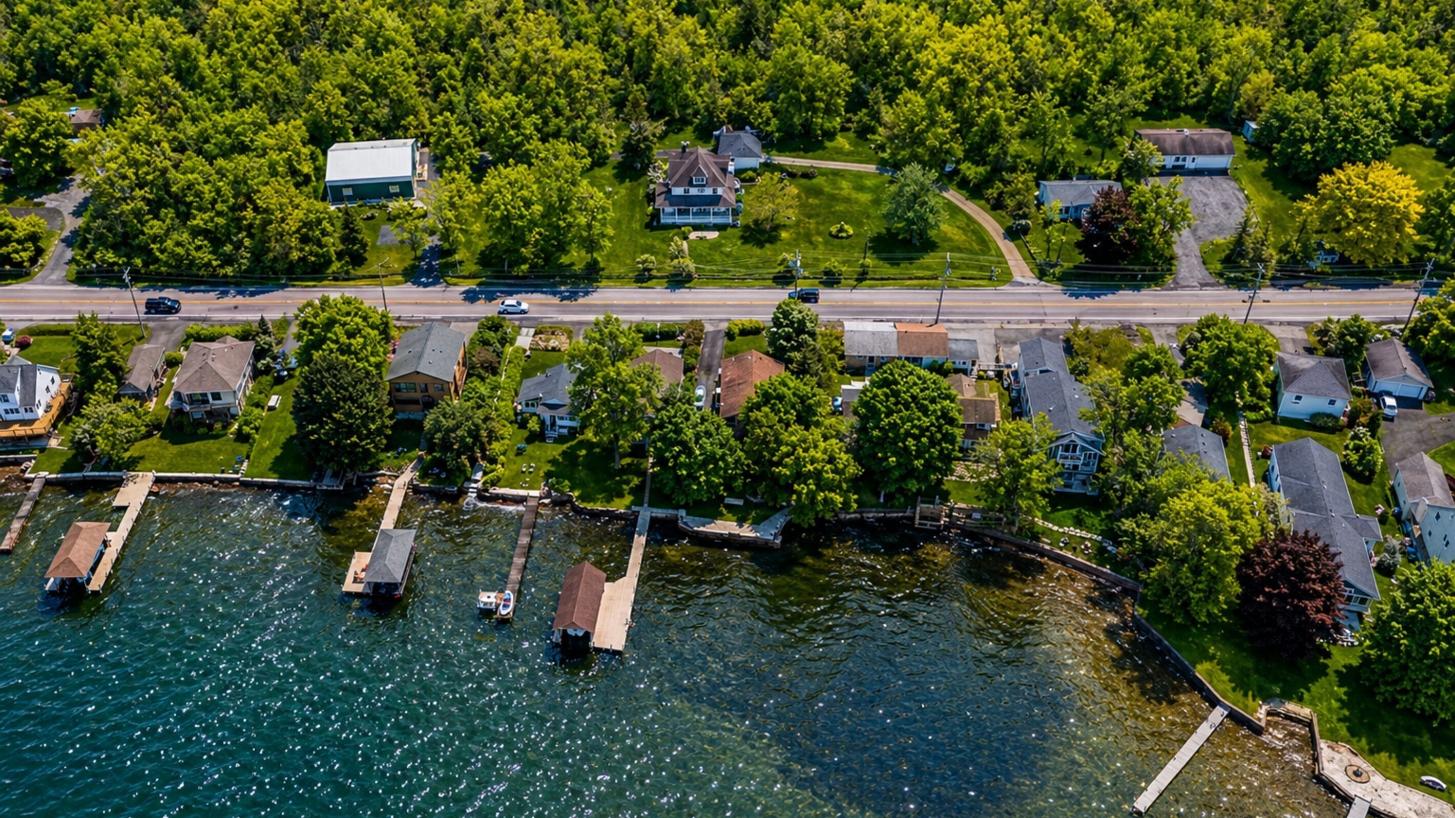 Vue aérienne d’un quartier résidentiel au bord d’un lac, avec des maisons, des quais et une route.