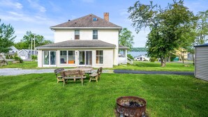 A two-story house with a covered porch, a fire pit, and a view of the water.
